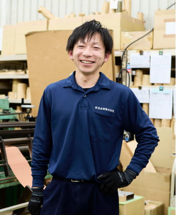 作業場をバックに満面の笑みを浮かべる男性